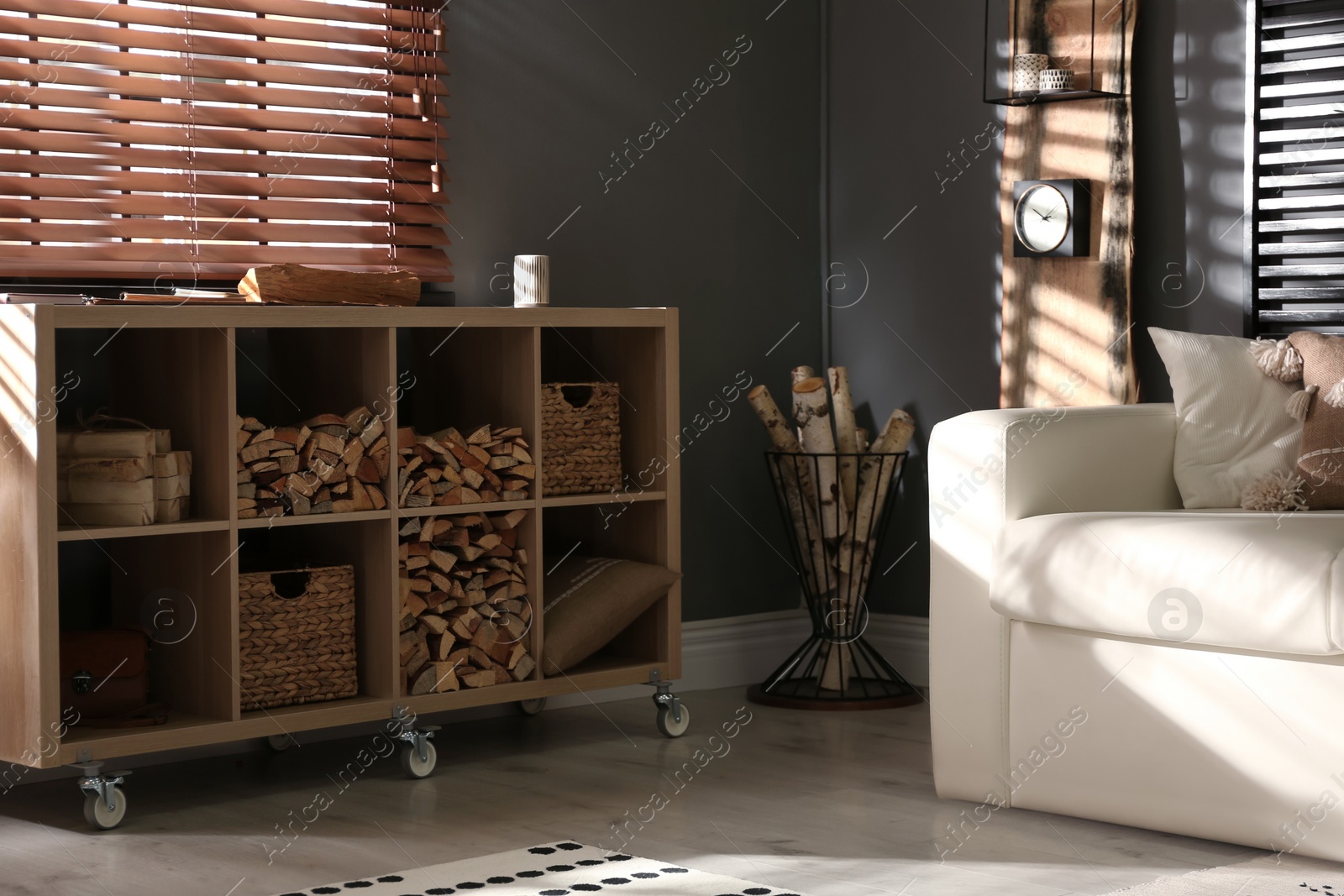 Photo of Shelving unit with stacked firewood and comfortable sofa in stylish room interior