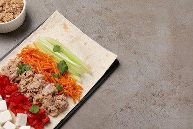 Photo of Delicious tortilla with tuna and vegetables on grey table, space for text. Cooking shawarma