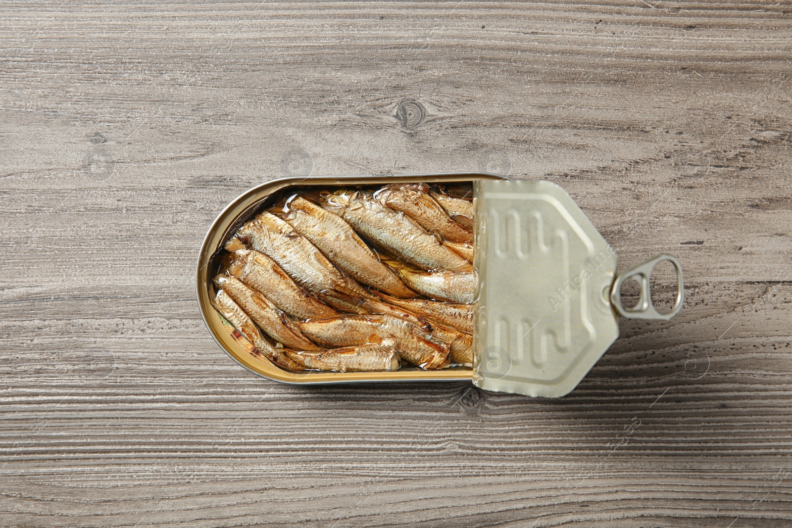 Photo of Open tin can of sprats on wooden background, top view