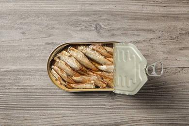 Photo of Open tin can of sprats on wooden background, top view