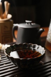 Photo of Cup with freshly brewed pu-erh tea on wooden tray, closeup