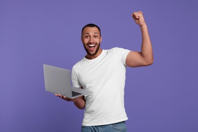 Photo of Happy young man with laptop on lilac background