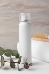 Photo of Dry shampoo spray, towel and eucalyptus on white wooden table