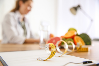 Clipboard, measuring tape and blurred nutritionist on background