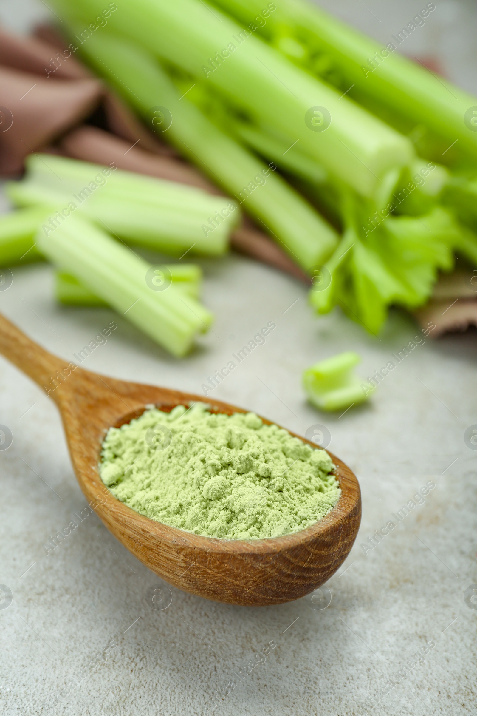 Photo of Natural celery powder in wooden spoon on grey table, closeup