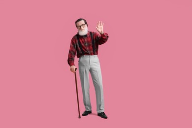 Photo of Senior man with walking cane waving on pink background