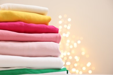 Photo of Stack of folded clothes on beige background with blurred lights, closeup. Space for text