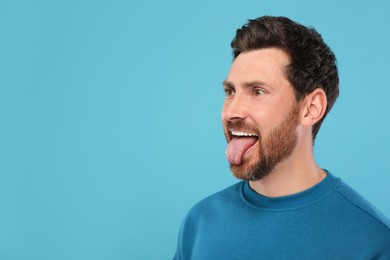 Man showing his tongue on light blue background, space for text
