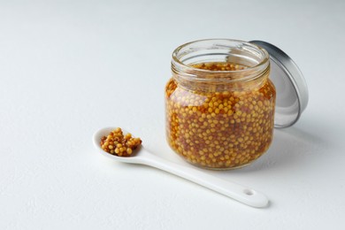 Photo of Jar and spoon with whole grain mustard on white table. Space for text