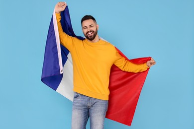 Young man holding flag of France on light blue background