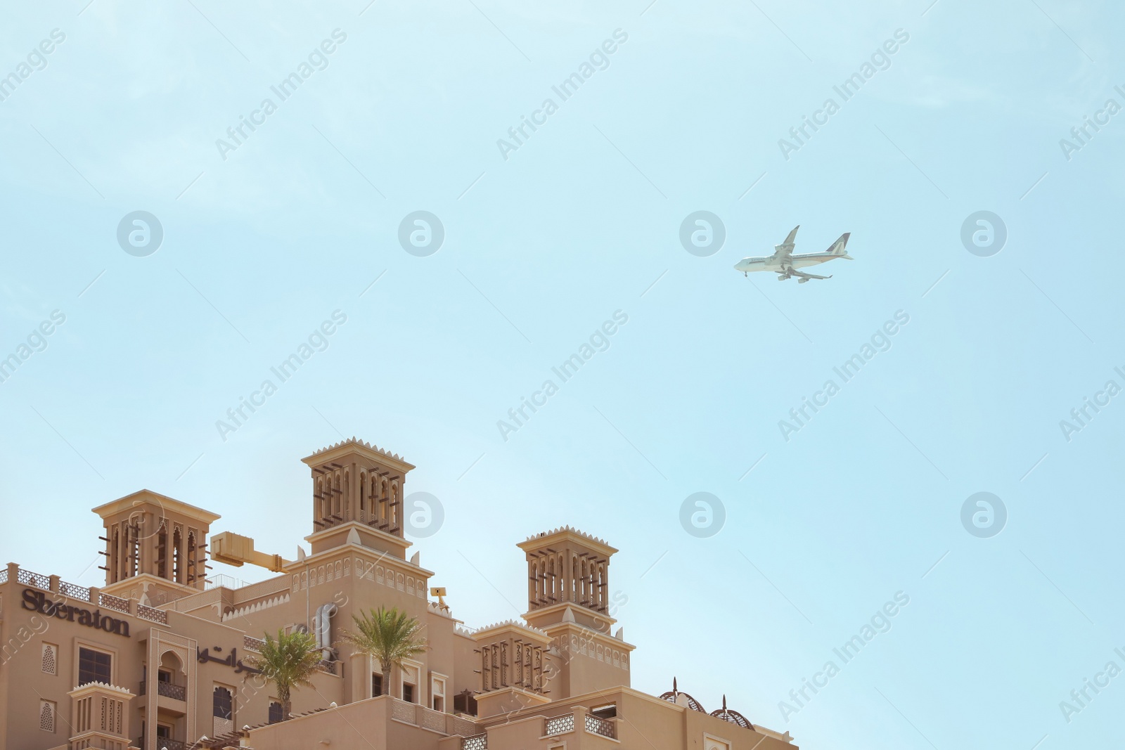 Photo of SHARJAH, UNITED ARAB EMIRATES - NOVEMBER 04, 2018: Modern airplane in sky over Sheraton resort on sunny day