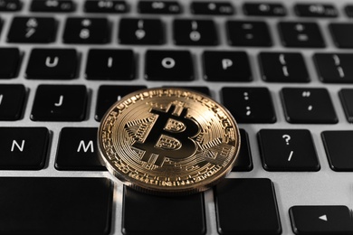 Photo of Golden bitcoin on computer keyboard, closeup. Digital currency