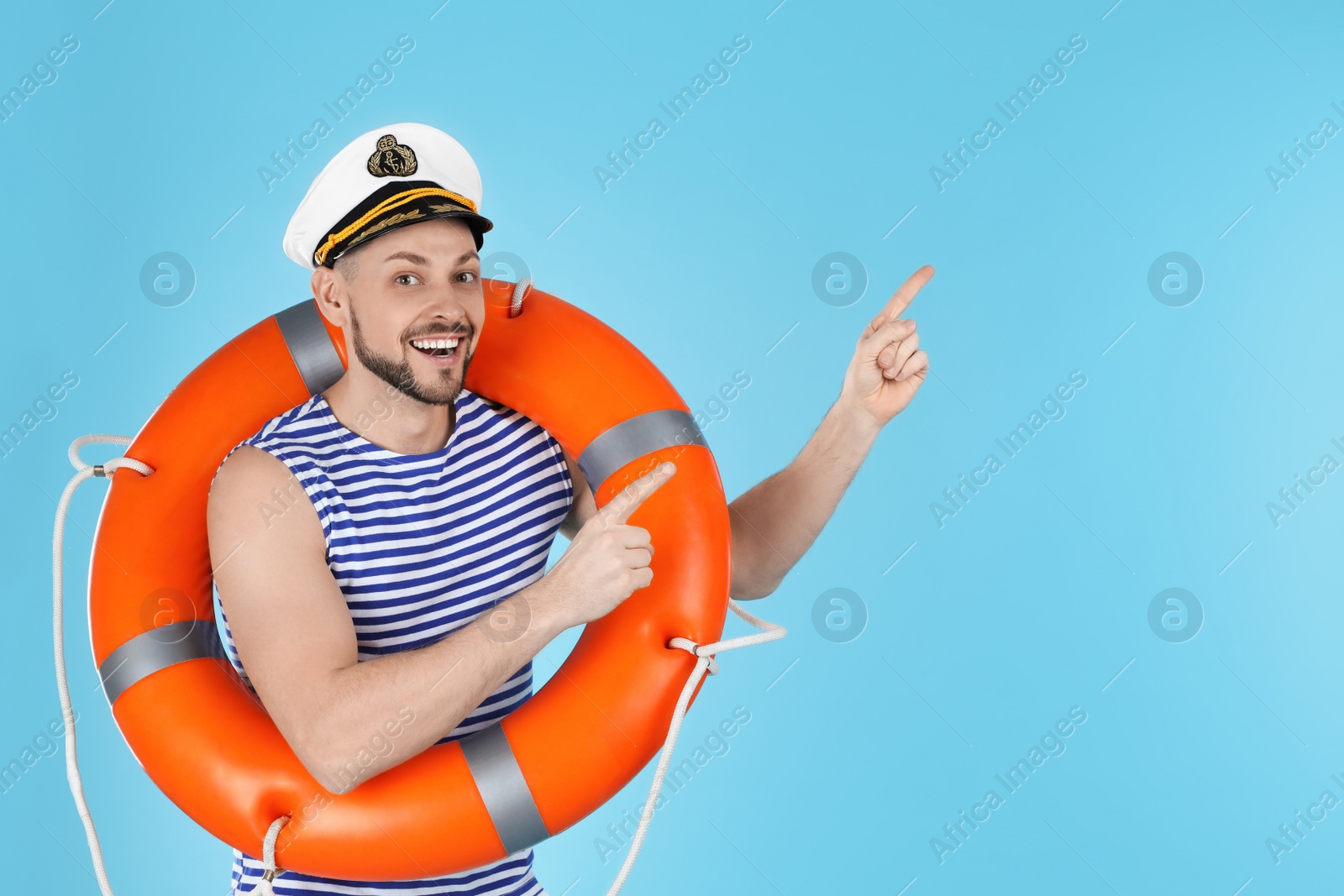 Photo of Happy sailor with orange life buoy pointing on light blue background, space for text