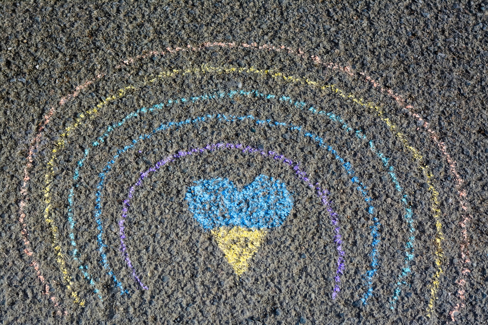 Photo of Rainbow with heart drawn by blue and yellow chalk on asphalt, top view