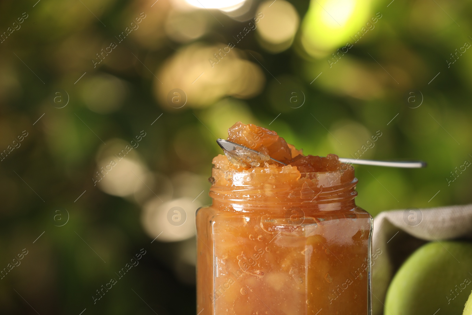 Photo of Glass jar with delicious apple jam against blurred background, closeup. Space for text