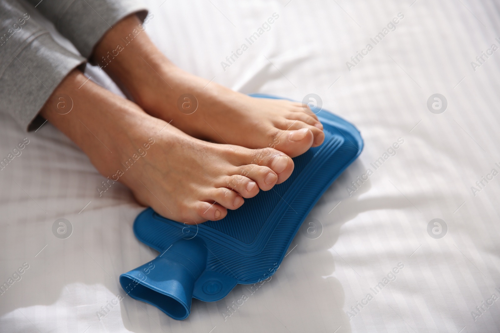 Photo of Man warming feet with hot water bottle on bed, closeup