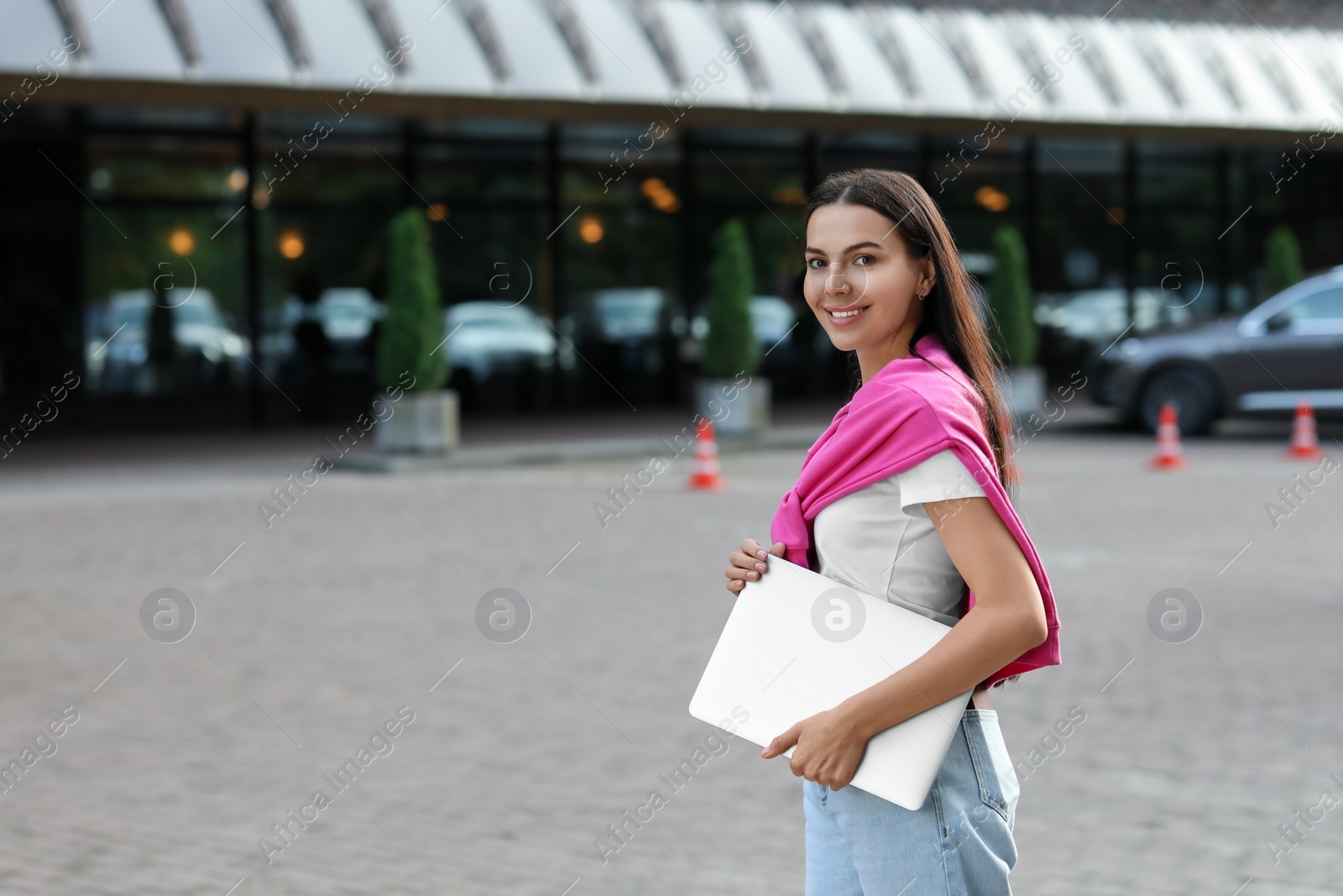 Photo of Happy young woman holding modern laptop on city street. Space for text