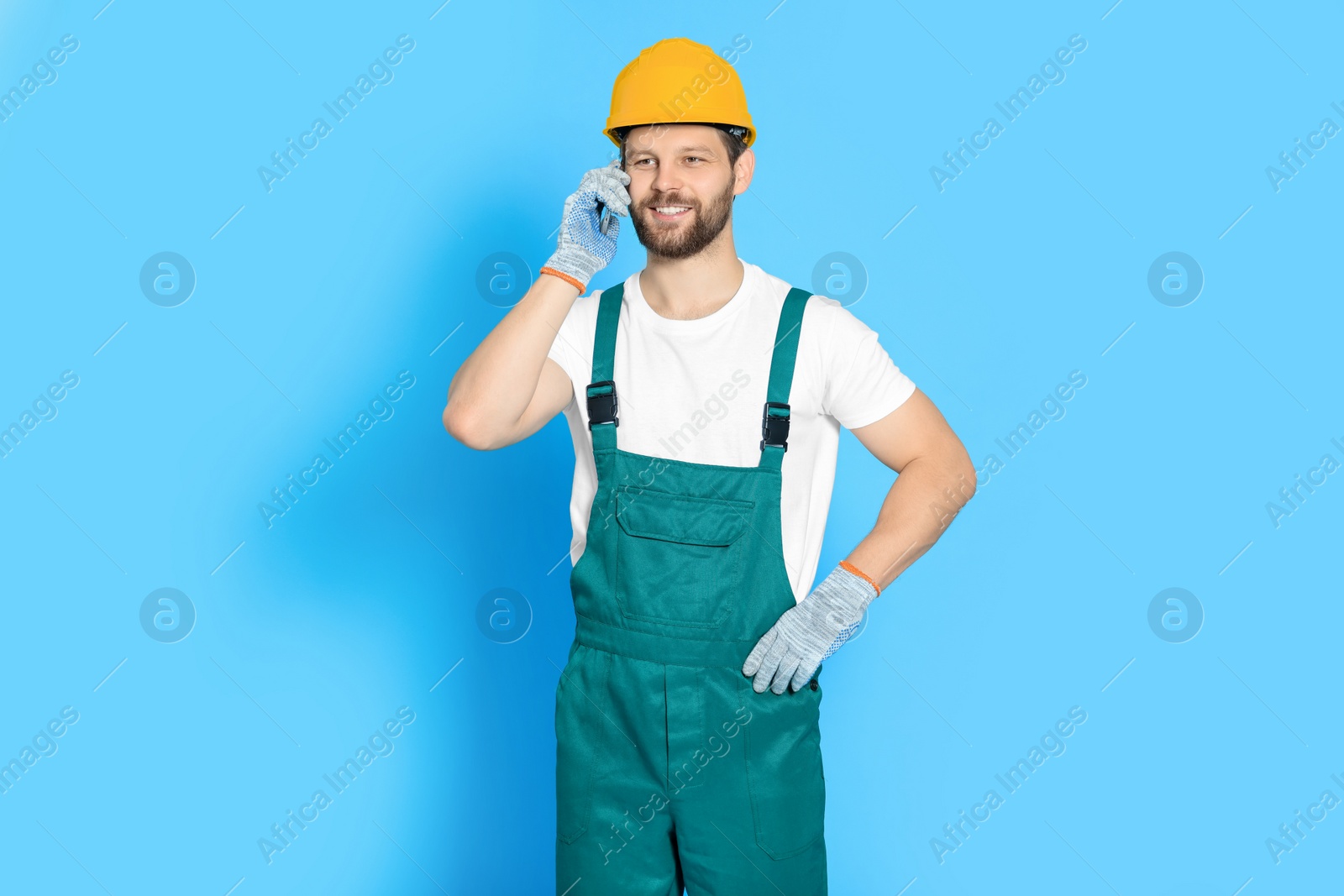 Photo of Professional repairman in uniform talking on smartphone against light blue background