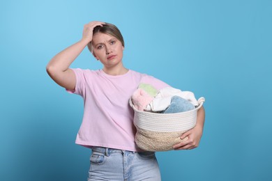 Tired woman with basket full of laundry on light blue background