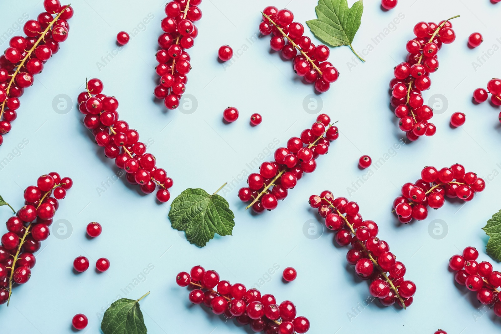 Photo of Delicious red currants and leaves on light blue background, flat lay