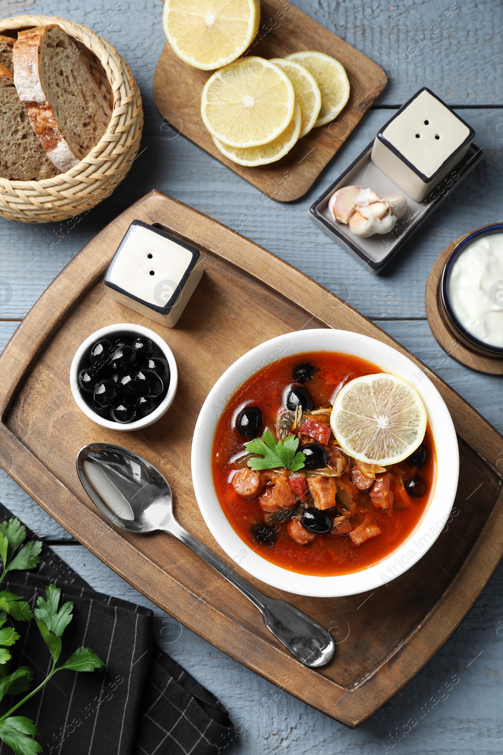 Photo of Meat solyanka soup with sausages, olives and vegetables served on grey wooden table, flat lay