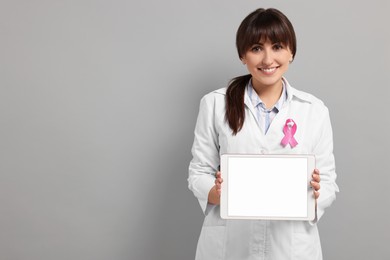 Photo of Mammologist with pink ribbon showing tablet on light grey background, space for text. Breast cancer awareness
