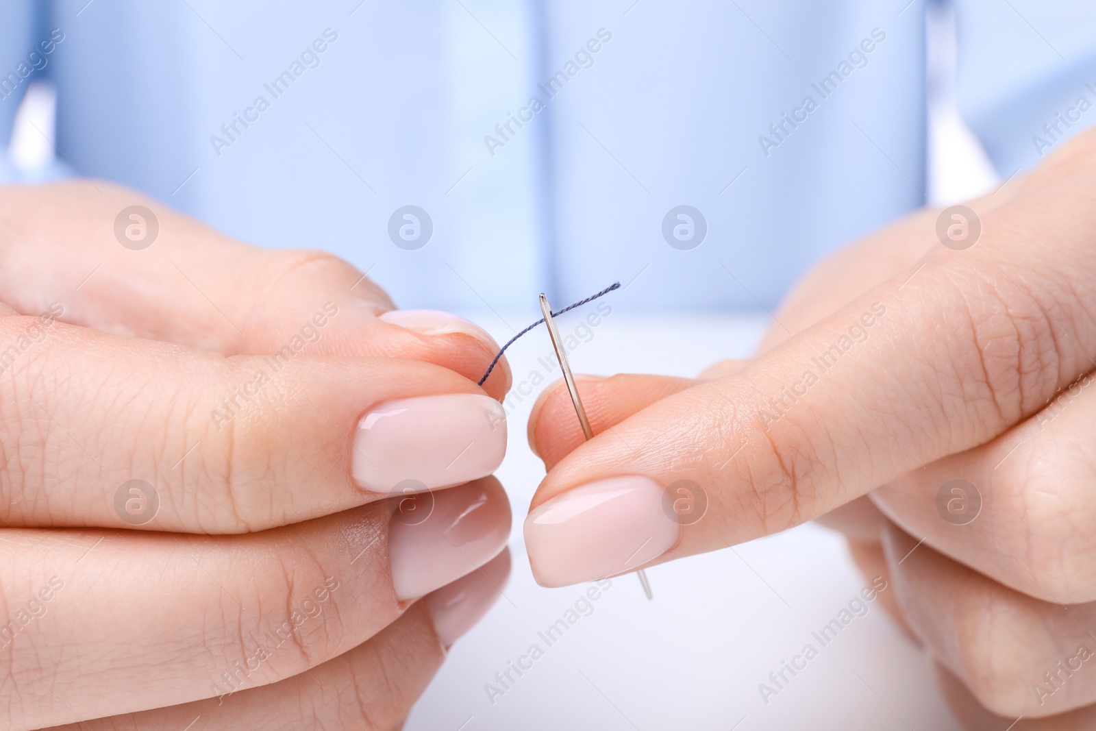 Photo of Woman threading sewing needle at table, closeup