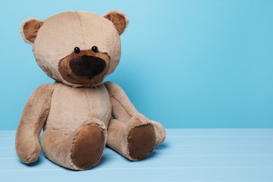 Photo of Cute teddy bear on wooden table against light blue background, space for text