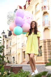 Beautiful young woman with color balloons on city street