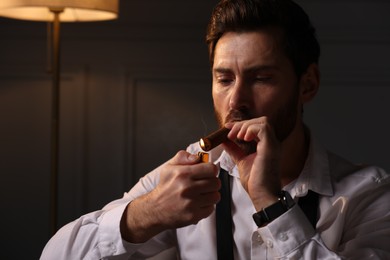 Handsome man lightning cigar at home. Space for text