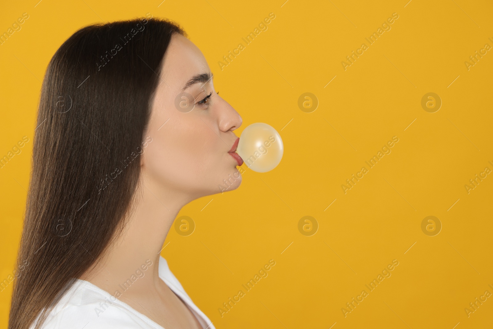 Photo of Beautiful young woman blowing bubble gum on yellow background. Space for text