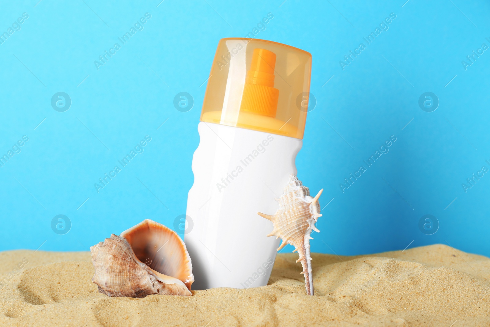 Photo of Suntan product, seashell and starfish on sand against light blue background
