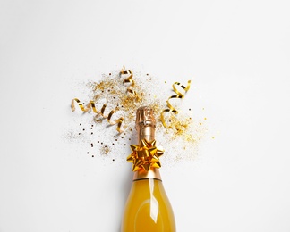 Photo of Bottle of champagne with gold glitter and bow on white background, top view. Hilarious celebration