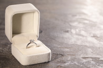 Photo of Beautiful engagement ring with gemstone in box on grey table. Space for text