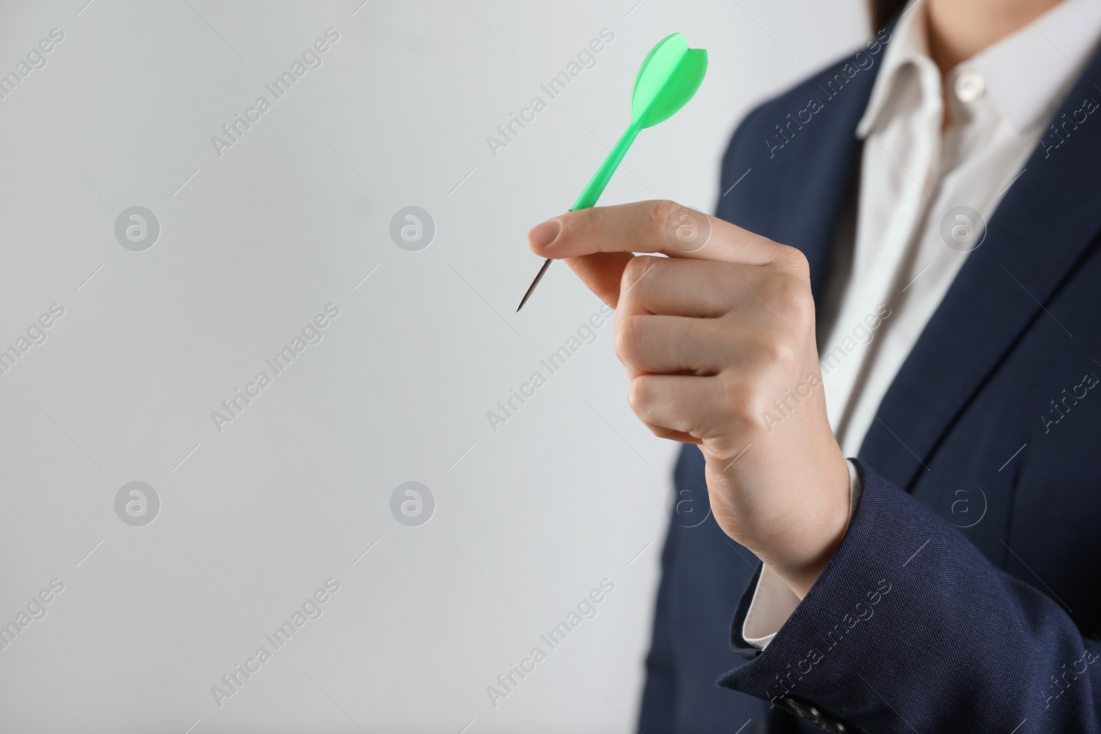 Photo of Businesswoman holding green dart on light background, closeup. Space for text