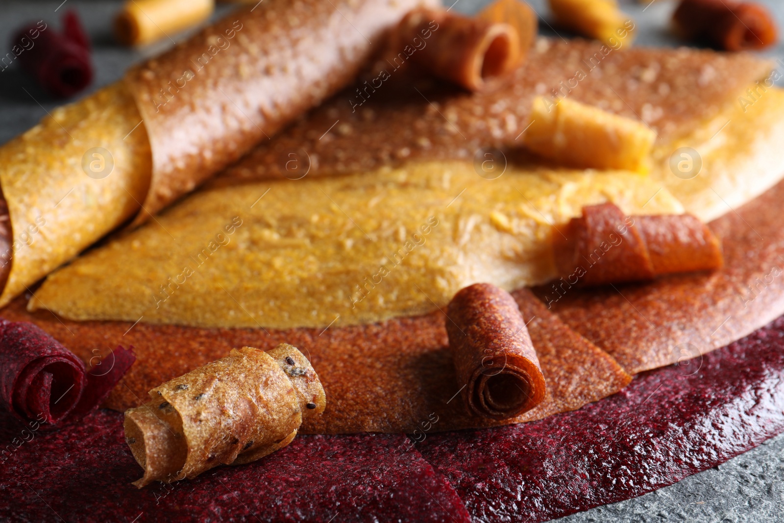 Photo of Delicious fruit leather rolls on grey table, closeup