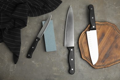 Sharpening stone and knives on grey table, flat lay