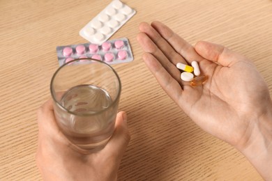 Man with glass of water and pills at wooden table, closeup