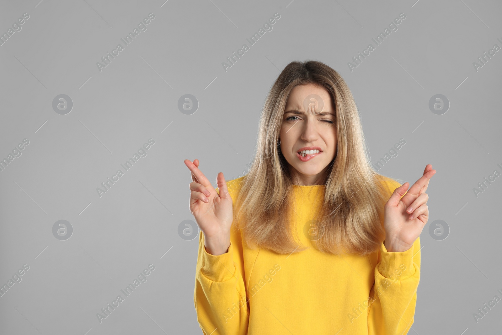 Photo of Woman with crossed fingers on light grey background, space for text. Superstition concept