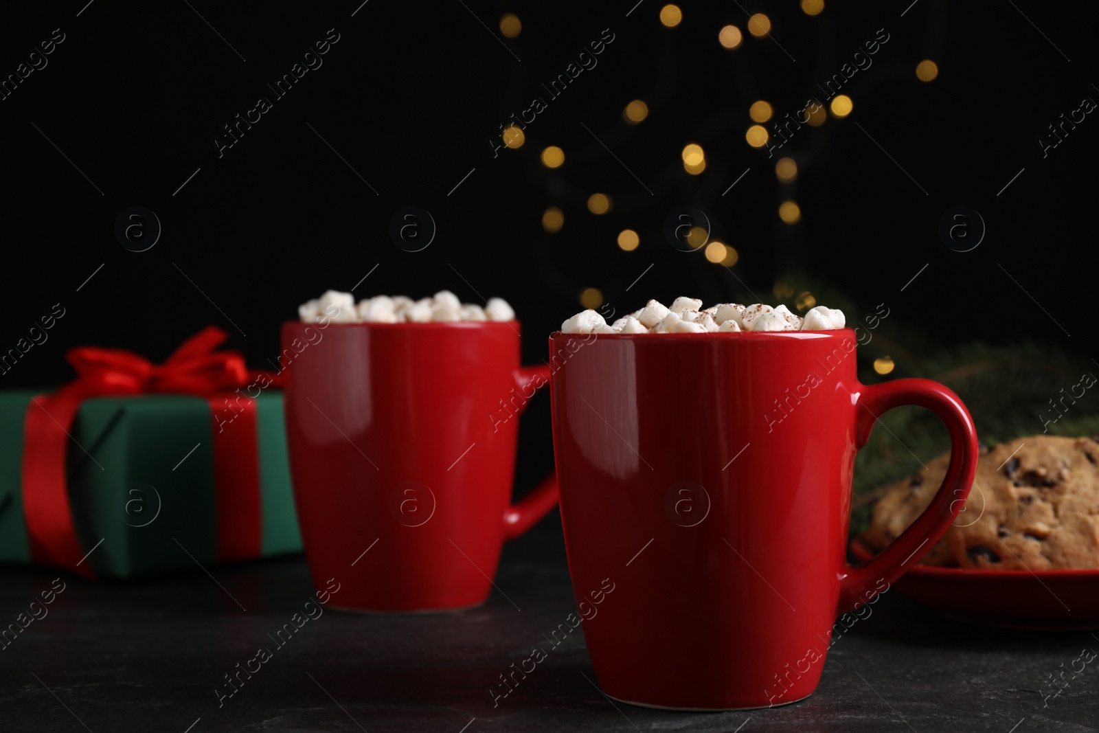 Photo of Delicious hot cocoa with marshmallows on black table against blurred lights, space for text