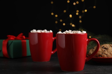 Delicious hot cocoa with marshmallows on black table against blurred lights, space for text