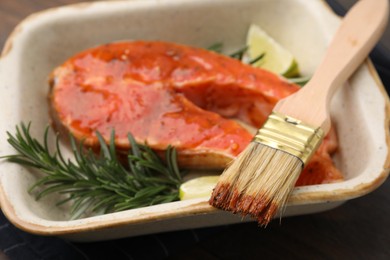 Photo of Fresh marinade, fish, rosemary, lime and brush on wooden table, closeup