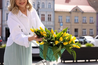 Photo of Woman with bicycle and bouquet of yellow tulips outdoors on city street, closeup