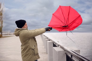 Photo of Man with red umbrella caught in gust of wind near river