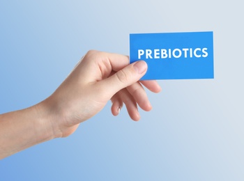 Image of Woman holding card with word PREBIOTICS on light blue background, closeup