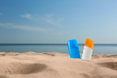 Photo of Bottles of sunblocks in beach sand near sea. Space for text