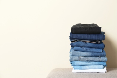 Photo of Stack of different jeans on ottoman against light background. Space for text