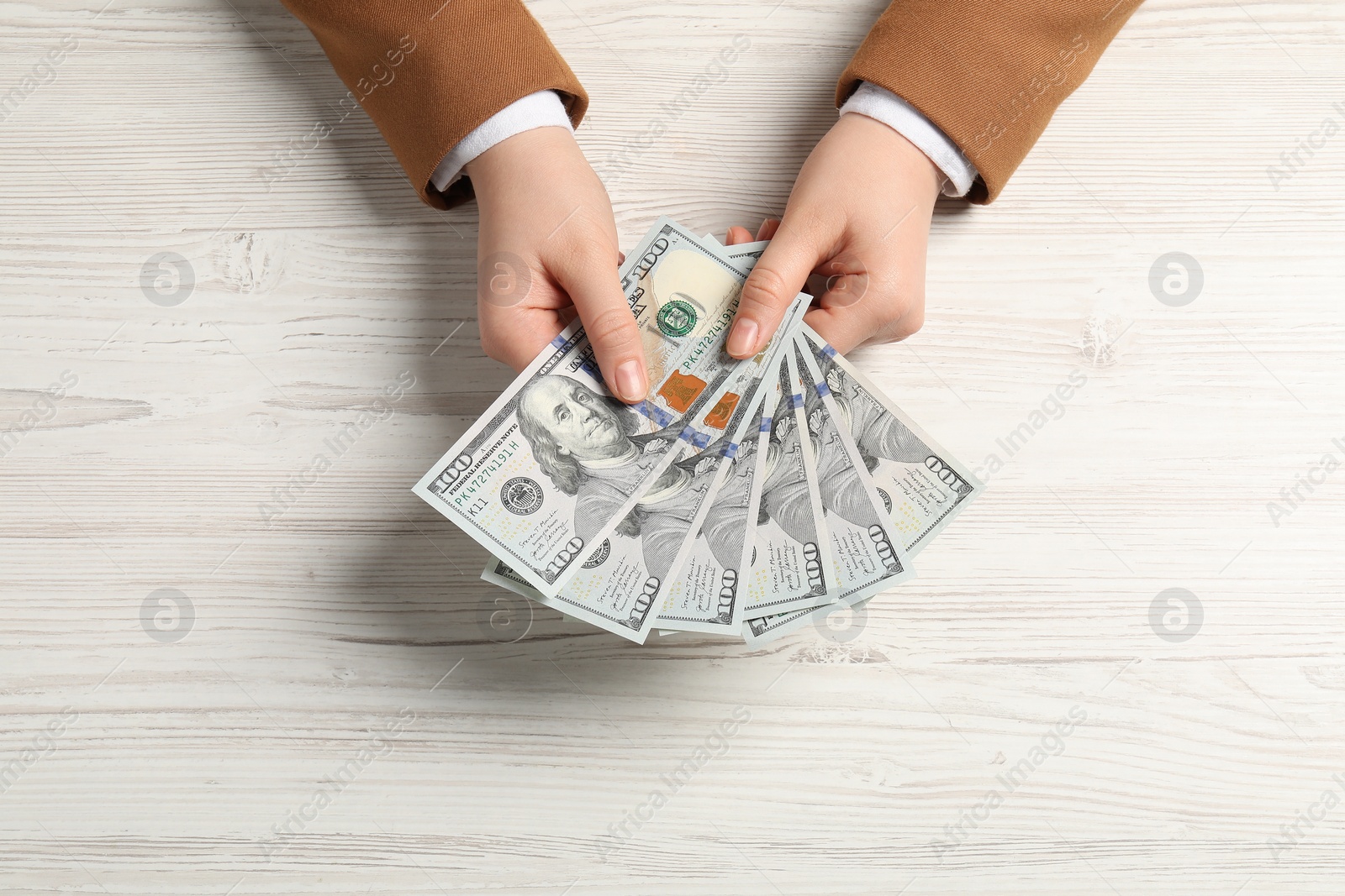 Photo of Money exchange. Woman holding dollar banknotes at white wooden table, top view