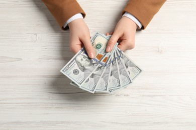 Money exchange. Woman holding dollar banknotes at white wooden table, top view