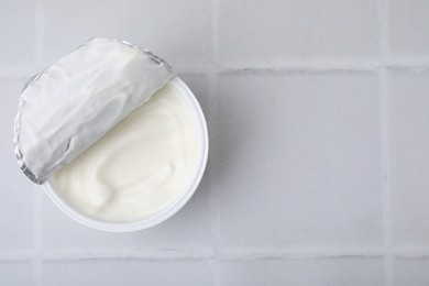 Photo of Delicious natural yogurt in plastic cup on white tiled table, top view. Space for text